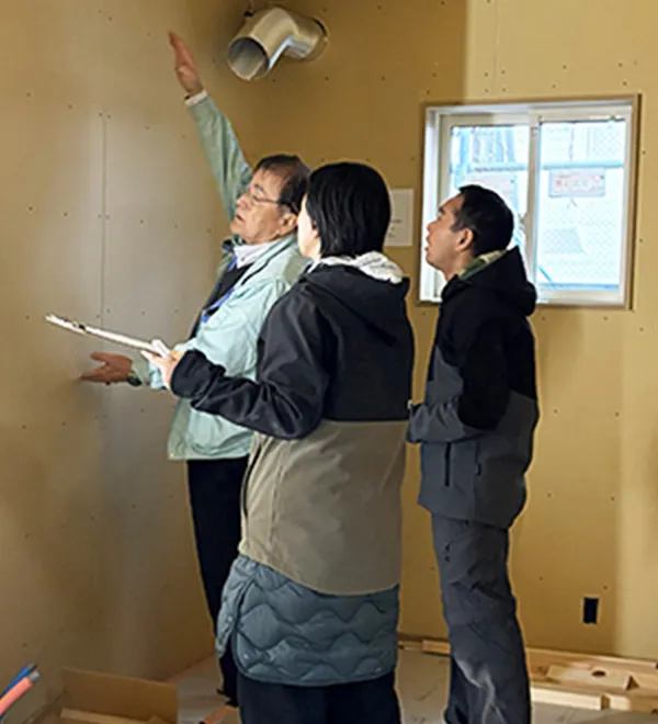 工事中の現場で天井付近を指さし説明しながら打合せをする3名の様子