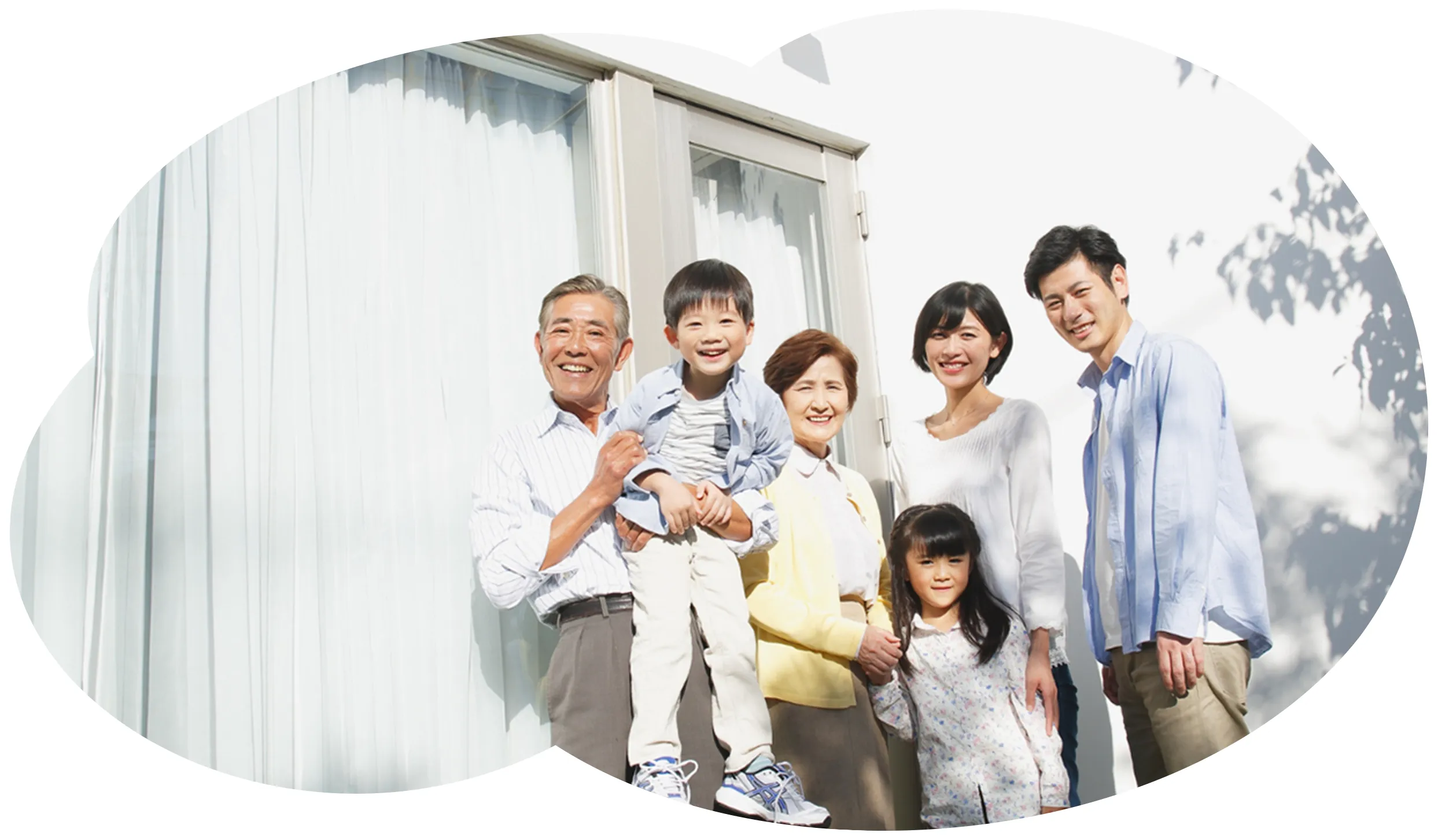 玄関前で笑顔の家族6人（祖父母・両親・子ども2人）と家の外観