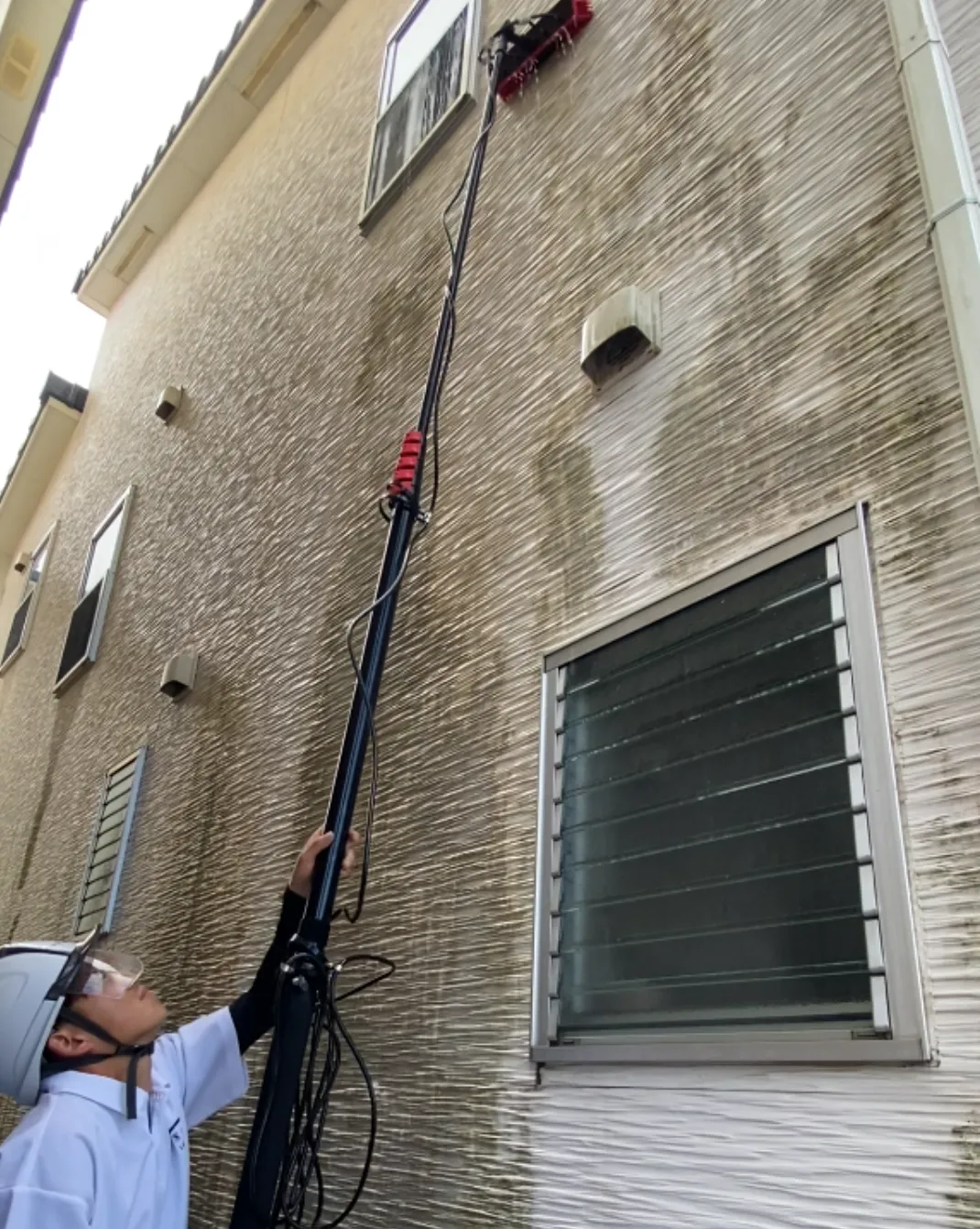 長尺ポールを使った建物の外壁清掃作業（石造り風の外壁の建物）