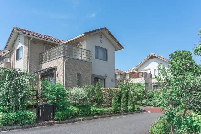 青空の下、手入れの行き届いた庭を持つモダンな一軒家が立ち並ぶ住宅地