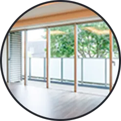 木製フローリングの室内から、大きなガラス戸越しに見える緑の木々と空（窓）