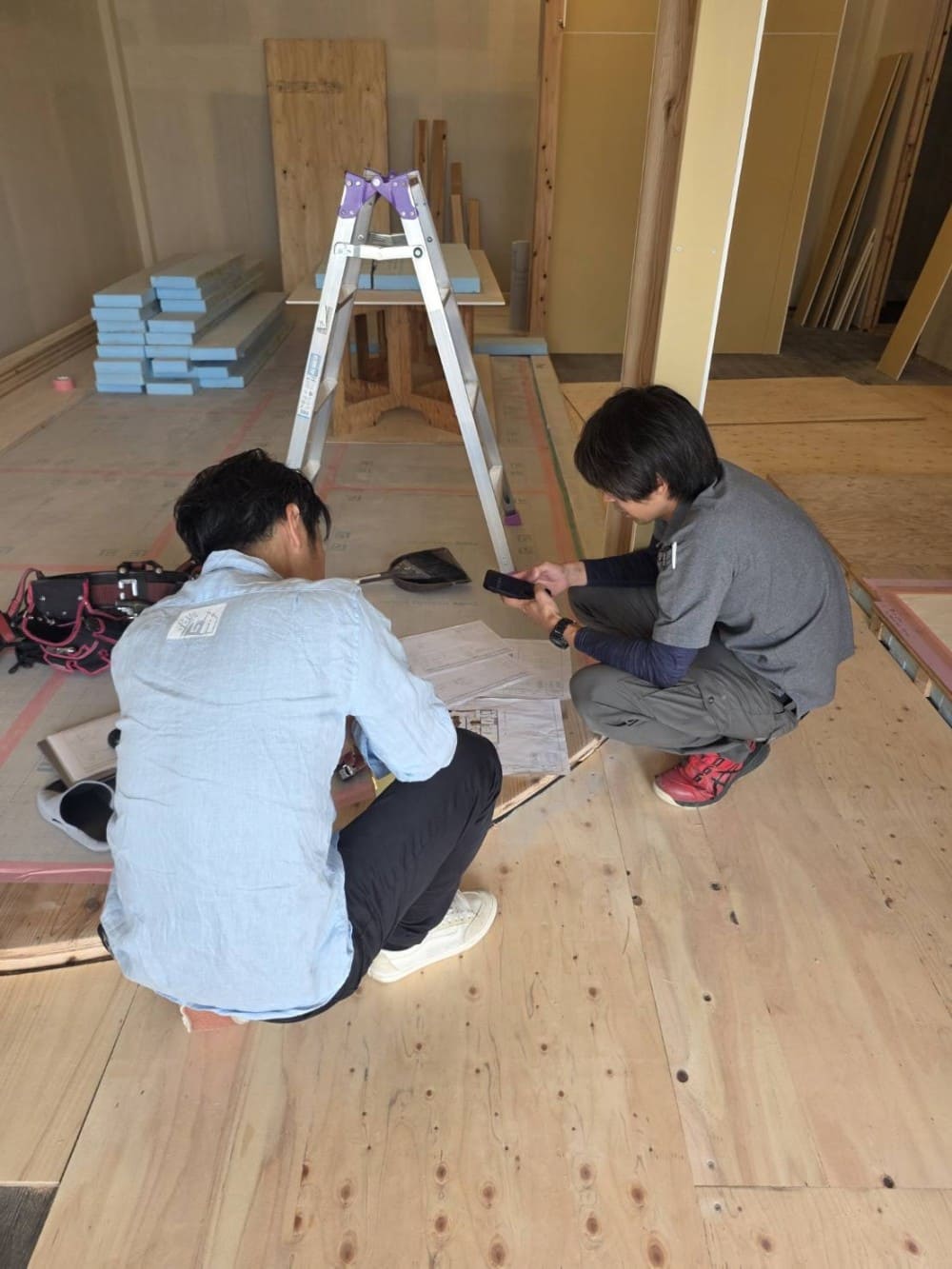 工事現場で天井・壁を指し示しながら打合せする3人の男性（メジャーやタブレットを持った施工・検査の様子）